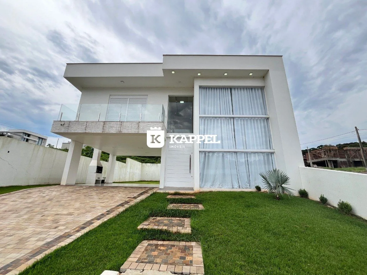 Fachada de uma residência moderna branca com jardim e calçada em Lajeado.