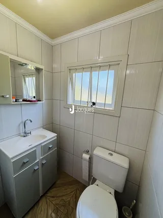 Foto interna de um banheiro com revestimento de azulejos brancos e piso de madeira.