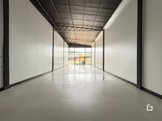Corredor interno com teto de estrutura metálica e paredes brancas.