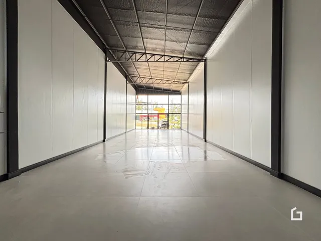 Corredor interno com teto de estrutura metálica e paredes brancas.