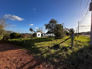 Vista externa de uma área rural com campo gramado e estrada de terra sob céu azul.