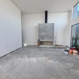 Foto de um ambiente interno vazio com piso de concreto e paredes brancas.