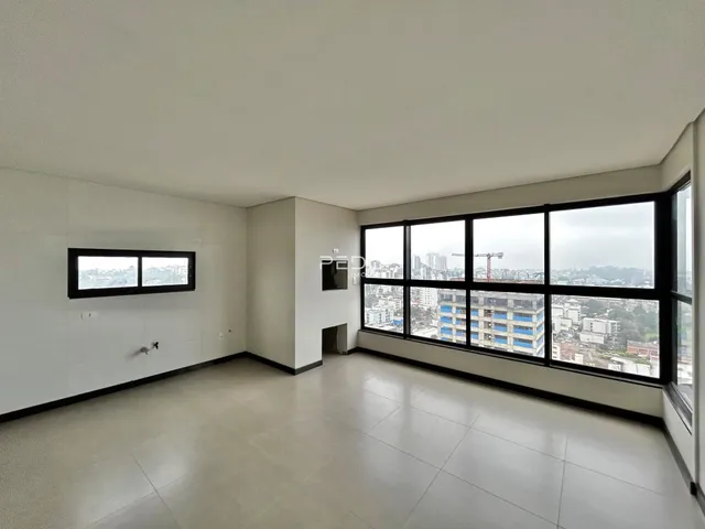 Ambiente interno de uma sala ampla com grandes janelas que oferecem vista da cidade.