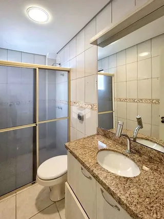 Banheiro com box de vidro e pia de granito.