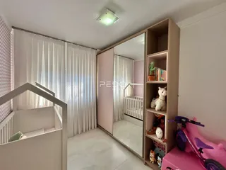 Quarto com cortinas brancas e estante de madeira na sala.