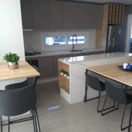 Vista de uma cozinha moderna com armários em tons de cinza e bancadas claras.
