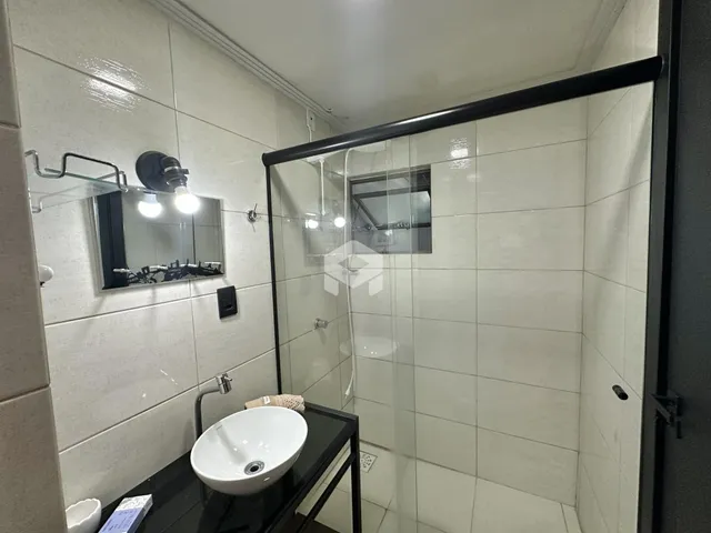 Banheiro com box de vidro e revestimento cerâmico branco.