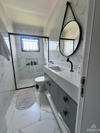 Banheiro com revestimento em mármore branco e espelho escuro.