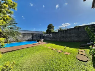 Vista externa de uma piscina e jardim com deck ao lado de uma parede de tijolos.