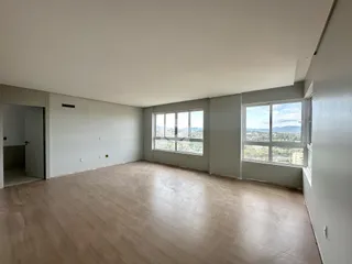 Imagem de uma sala de estar ampla com piso de madeira clara e grandes janelas.