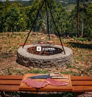 Foto de um ambiente externo com uma estrutura de pedra e carne em uma tábua, com uma paisagem de floresta ao fundo.