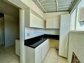 Vista interna de uma cozinha com armários brancos e bancada preta.