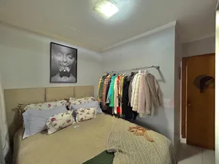Quarto com cama e roupas penduradas na parede.