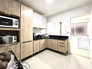 Vista interna de uma cozinha moderna com armários de madeira clara e revestimento branco.