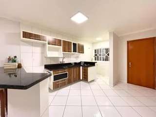 Vista da cozinha com armários de madeira e bancadas escuras.