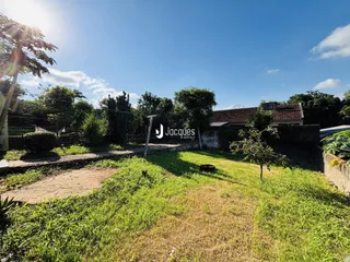 Vista externa de um terreno gramado com cerca de madeira e uma casa ao fundo.
