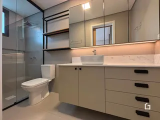 Banheiro moderno com box de vidro e armários brancos.