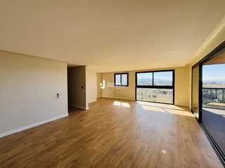 Ambiente interno de uma sala de estar ampla com piso de madeira clara.