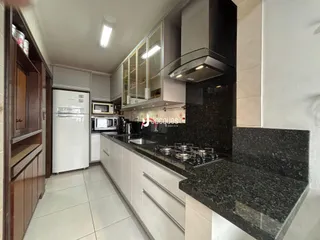 A cozinha moderna apresenta armários brancos e bancadas escuras.
