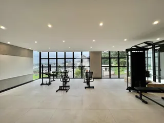 Interior de uma área comum com equipamentos de ginástica e grandes janelas.