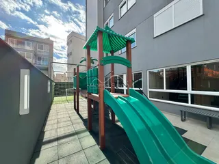 Área externa com playground verde e piso de ladrilhos.