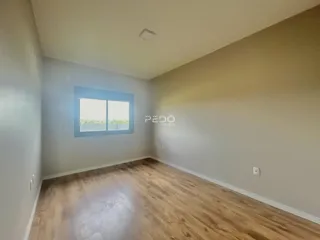 Ambiente interno de uma sala com piso de madeira clara e janela.