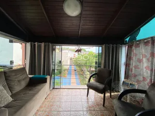 Sala de estar com sofá e cadeiras de madeira em um ambiente com piso de cerâmica.
