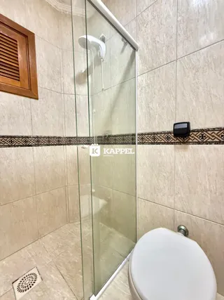 Foto interna de um banheiro com revestimento de azulejos brancos e box de vidro.