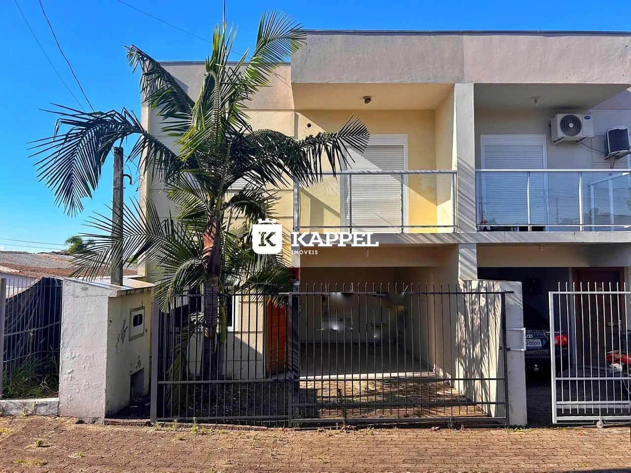 Fachada de um prédio residencial em Lajeado, Brasil, com cerca e palmeira em primeiro plano.