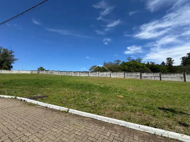 Vista externa de um campo gramado com uma cerca de concreto ao fundo sob um céu azul.