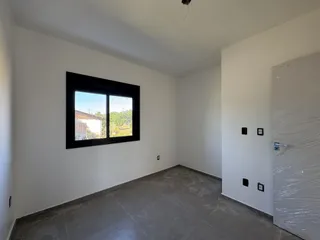 Vista interna de uma sala ampla com paredes brancas e piso de porcelanato cinza.