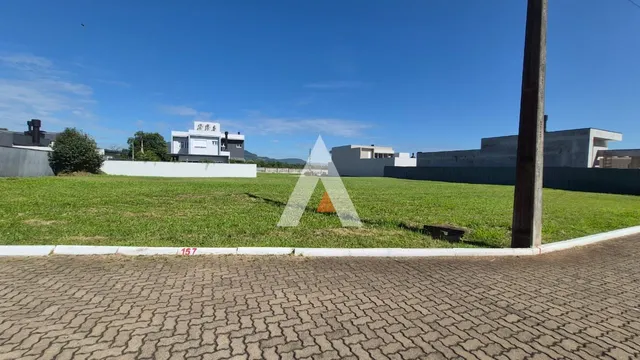 Vista externa de um terreno gramado com edificações ao fundo sob céu azul.