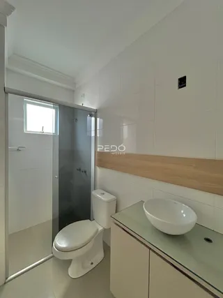 Interior de um banheiro com revestimento cerâmico e louças brancas.