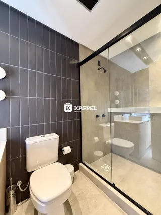 Banheiro com box de vidro e revestimento de azulejos escuros.