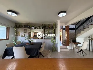 Uma sala de jantar com mesa escura e cadeiras brancas é visível na área comum da residência.