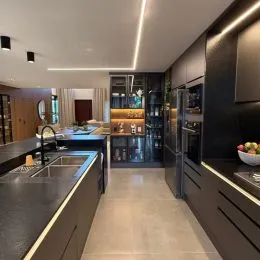 Foto interna de uma cozinha com armários escuros e bancadas.