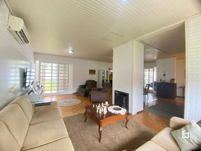 Sala de estar com piso de madeira e grandes janelas iluminando o ambiente.