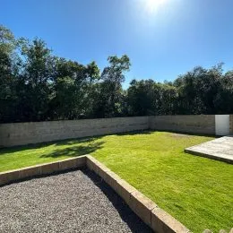 Área externa com gramado verde e vegetação densa ao fundo.