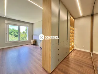 Sala de estar com piso de madeira e grande janela mostrando a vegetação externa.