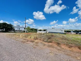 Vista externa de uma propriedade com terreno aberto e estruturas ao fundo.