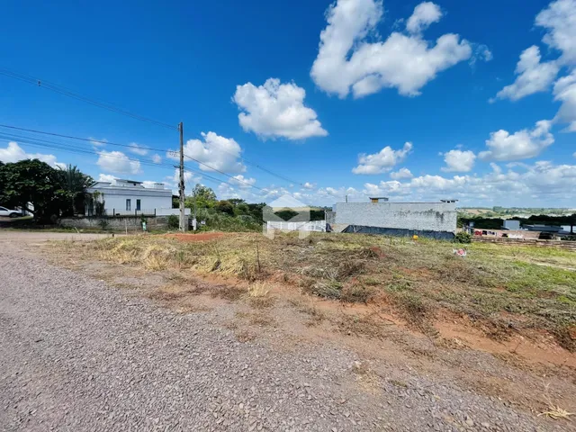 Vista externa de uma propriedade com terreno aberto e estruturas ao fundo.