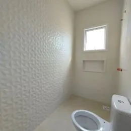 Foto interna de um ambiente com parede texturizada e vaso sanitário branco.