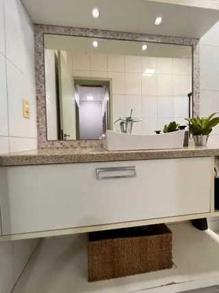 Foto de uma bancada de banheiro com espelho e armário branco.