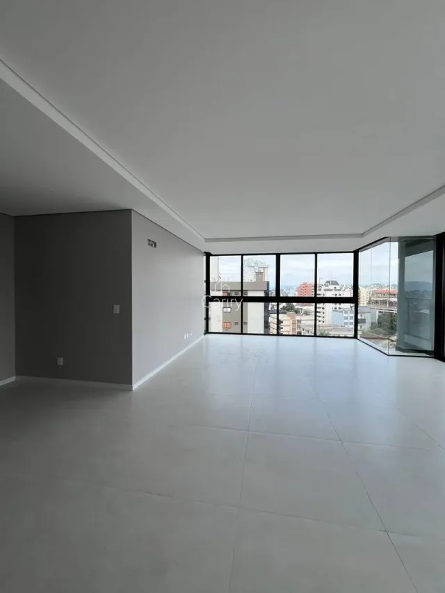 Vista interna de um ambiente amplo com piso claro e grandes janelas.