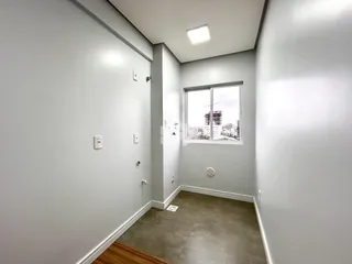 Vista de um corredor interno com paredes brancas e uma janela.