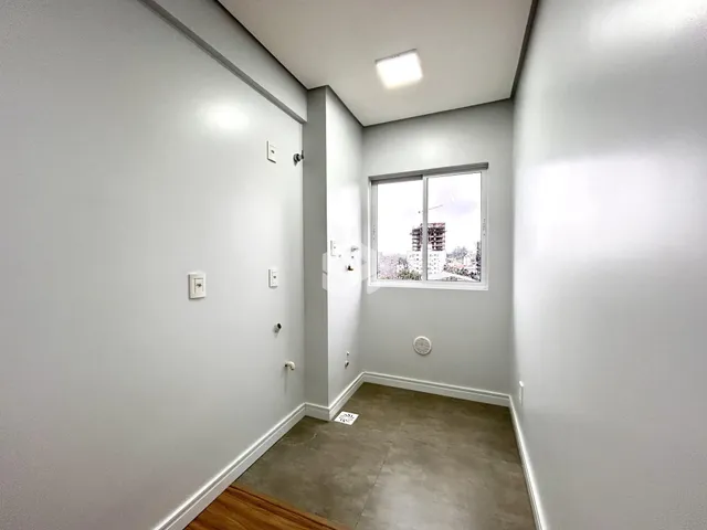 Vista de um corredor interno com paredes brancas e uma janela.