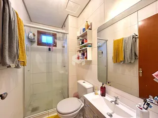 Banheiro com box de vidro, vaso sanitário e bancada branca.