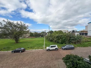 Vista externa de um terreno gramado com árvores e carros estacionados.