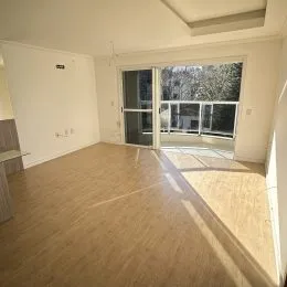 Sala de estar ampla com piso de madeira clara e porta de vidro que dá para o exterior.