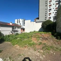 Vista externa de um edifício com vegetação e terreno baldio em primeiro plano.